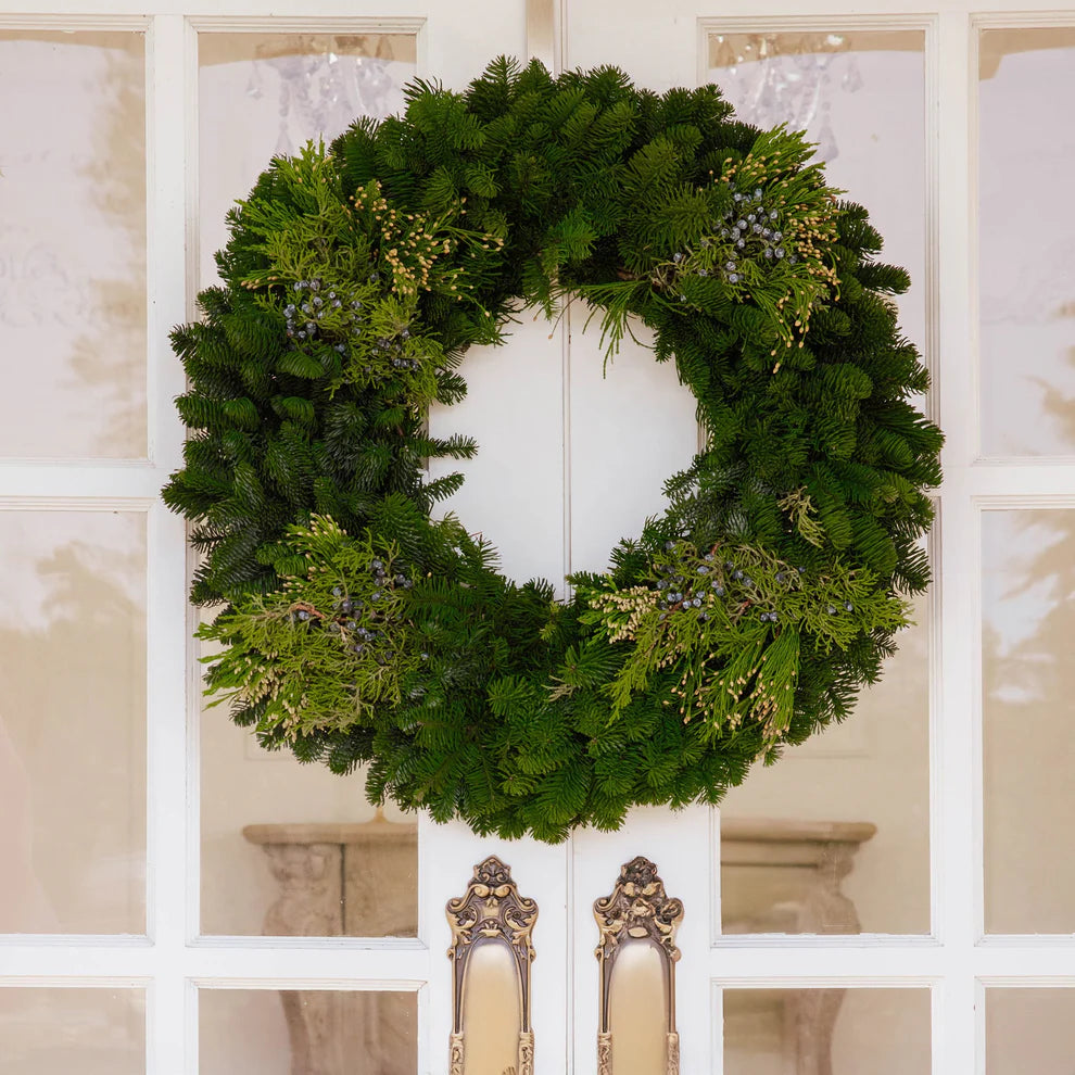 Fresh evergreen wreath on a white door with decorative frames
