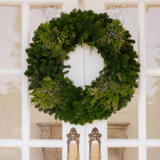 Fresh evergreen wreath on a white door with decorative frames
